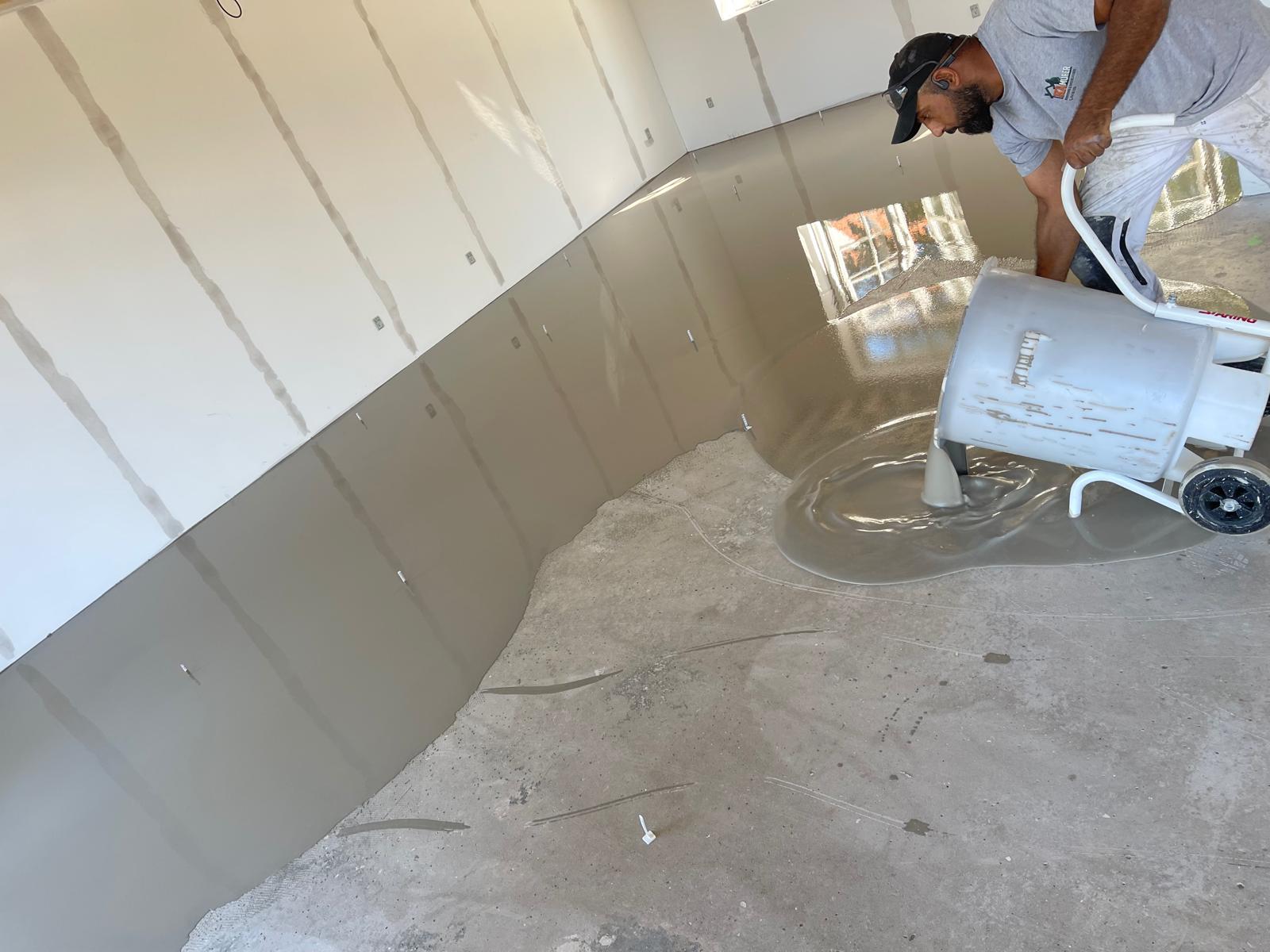 Håndværker fra KA MURER hælder flydespartel ud på betongulv under renovering
