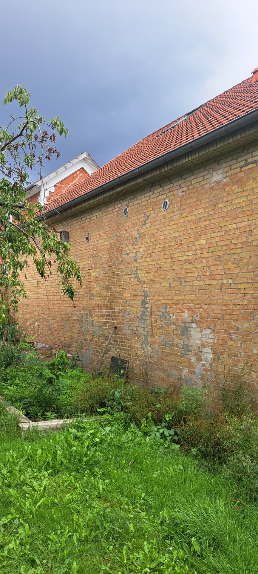 Lang murstensmur før renovering med fugtskjolder og gamle lapninger